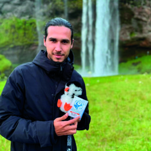 Frank holding his adopted LOÐVINIR puffin plush named Lundi in front of Skógafoss waterfall in Iceland